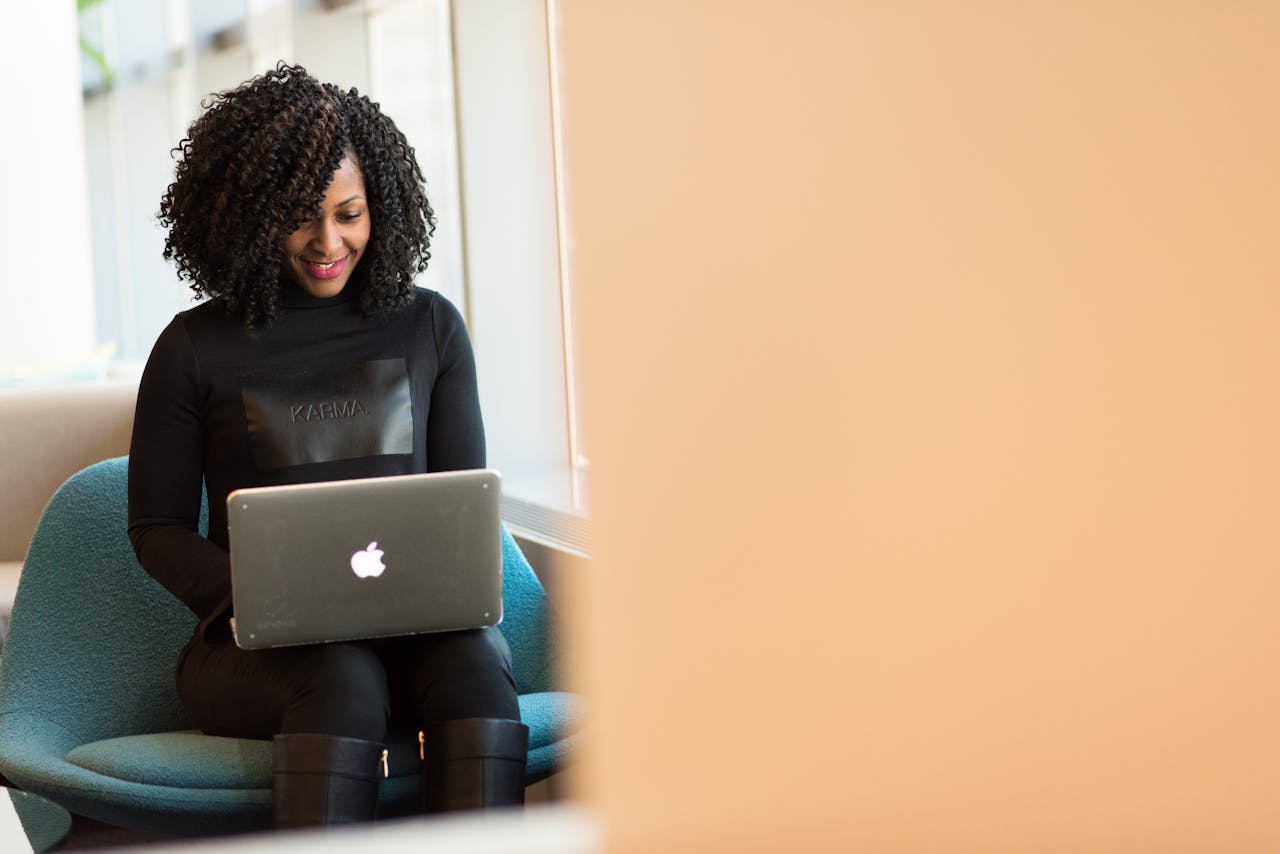 story-02 African American woman happily working on a laptop in a modern office setting.